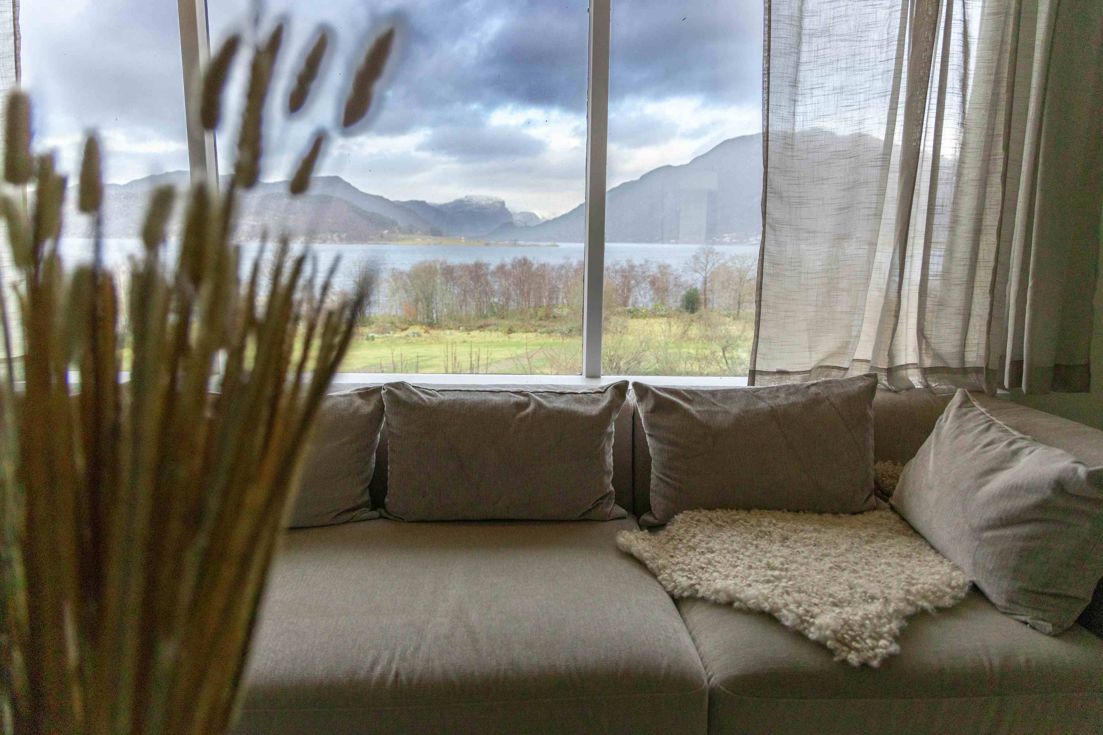 A living room in a hoilday home. Decorated in cream and white in a nordic style. Views of the fjord out the window. The photo shows a sofa, a chair, a coffee table and a book case. Holiday house near Lauvvik
