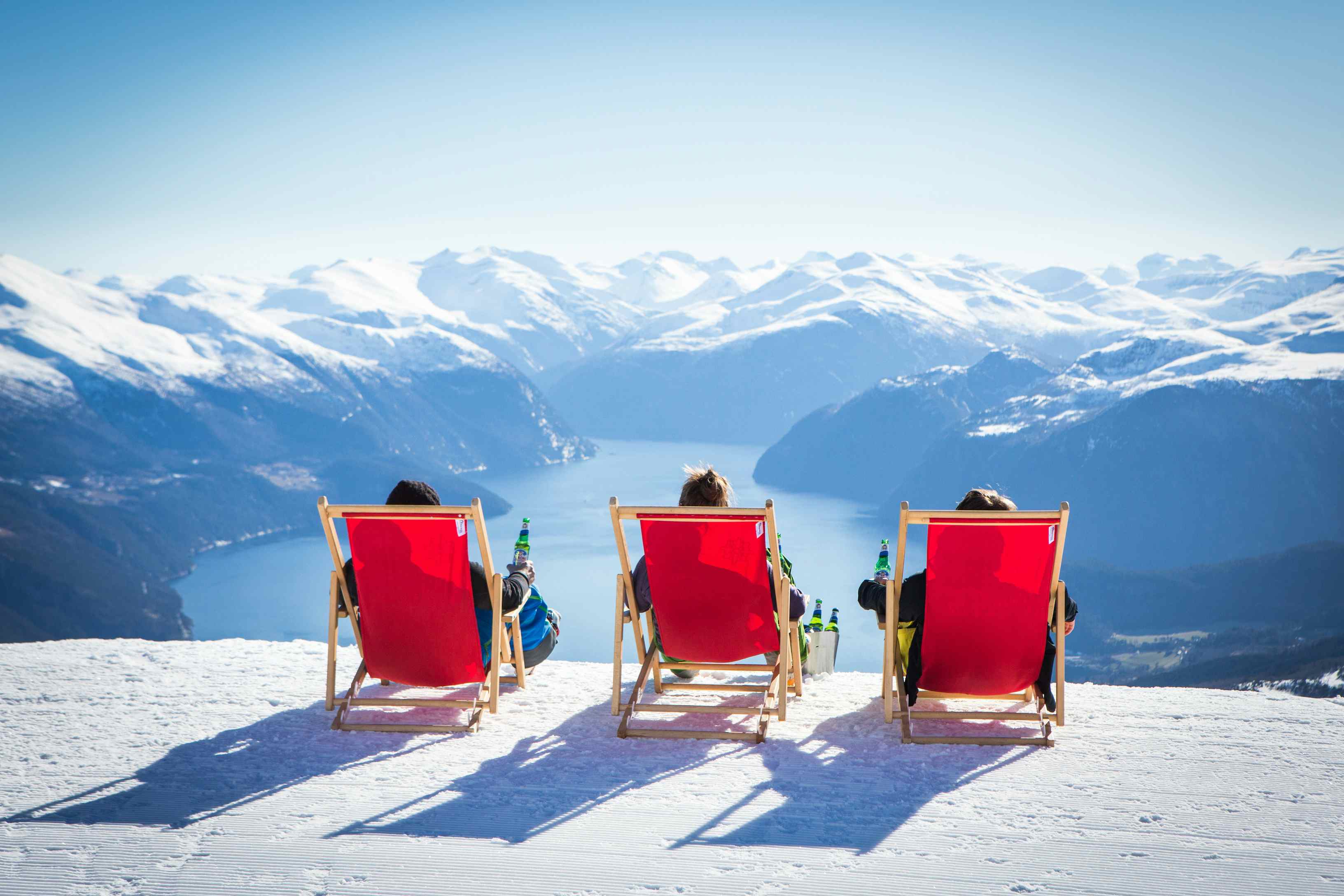 Tre røde stoler på strandafjellet med utsikt i et vinterdekket landskap over fjorden