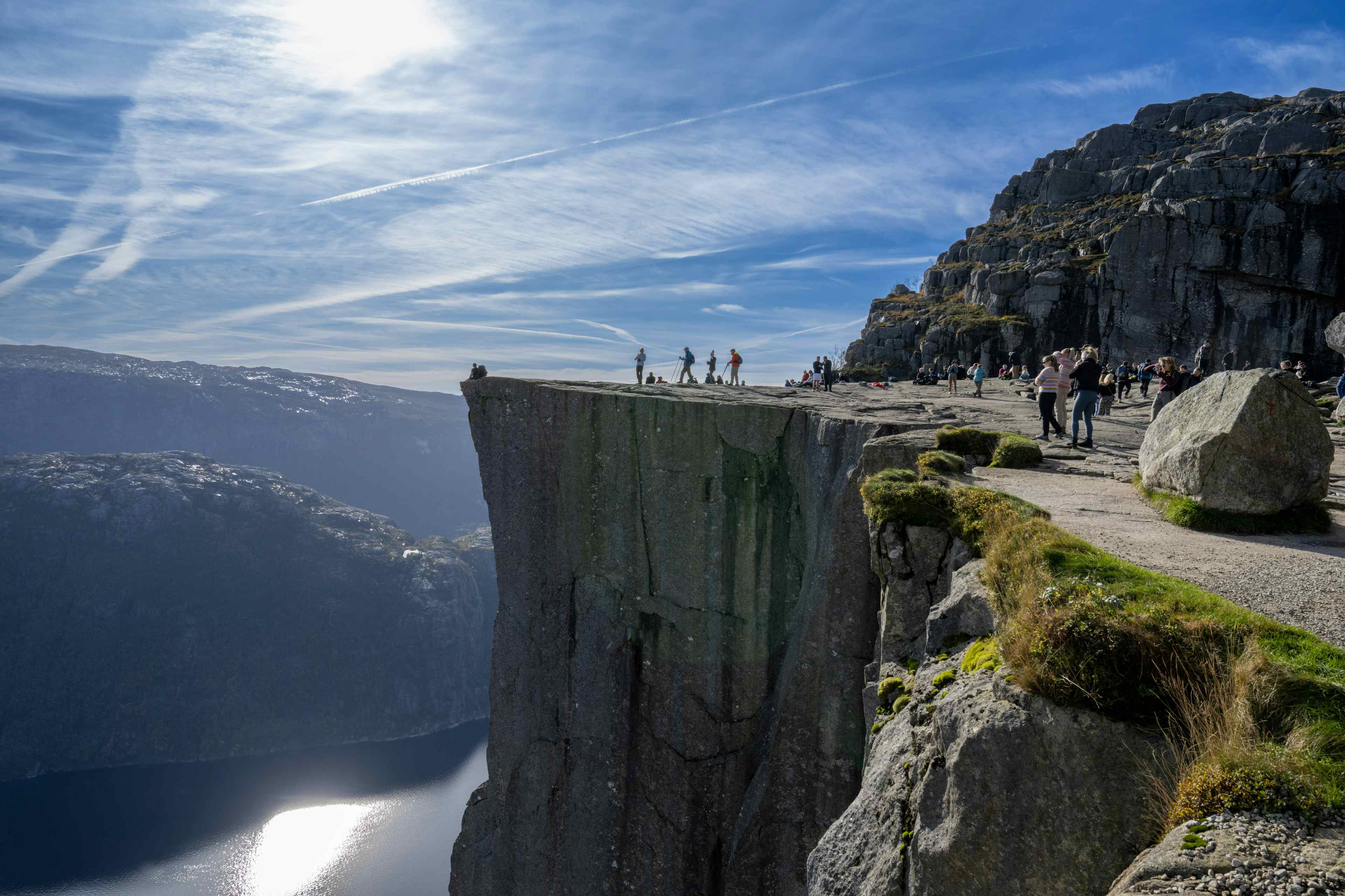 People standing on a mountain plateaut more than 600 metres above fjord level. Blue sky and sunny day. Steep mountains and fjord. Guided hike to Preikestolen