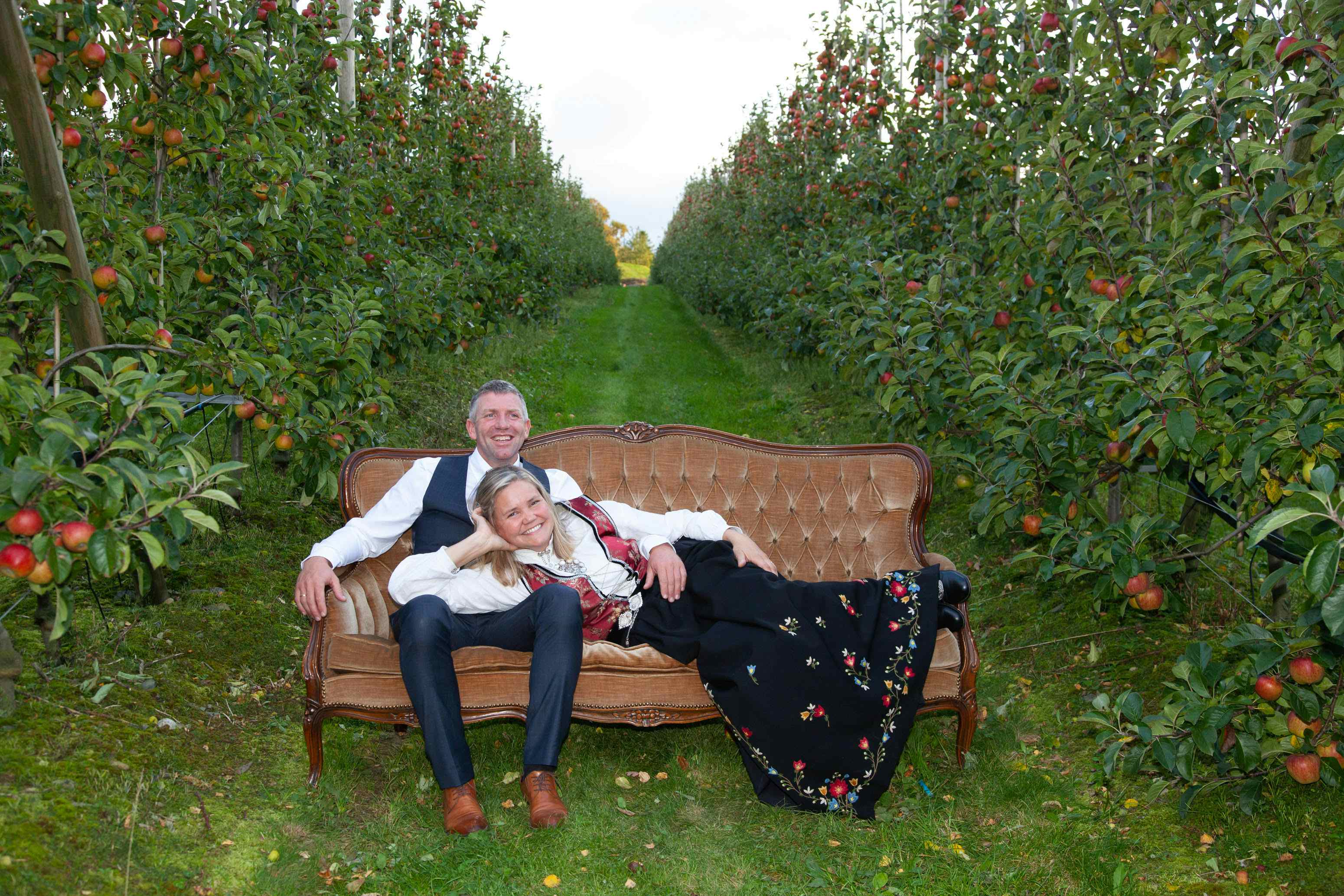 Eierne Kristen og Anne Norunn festpynta i en sofa blant epletrærne.