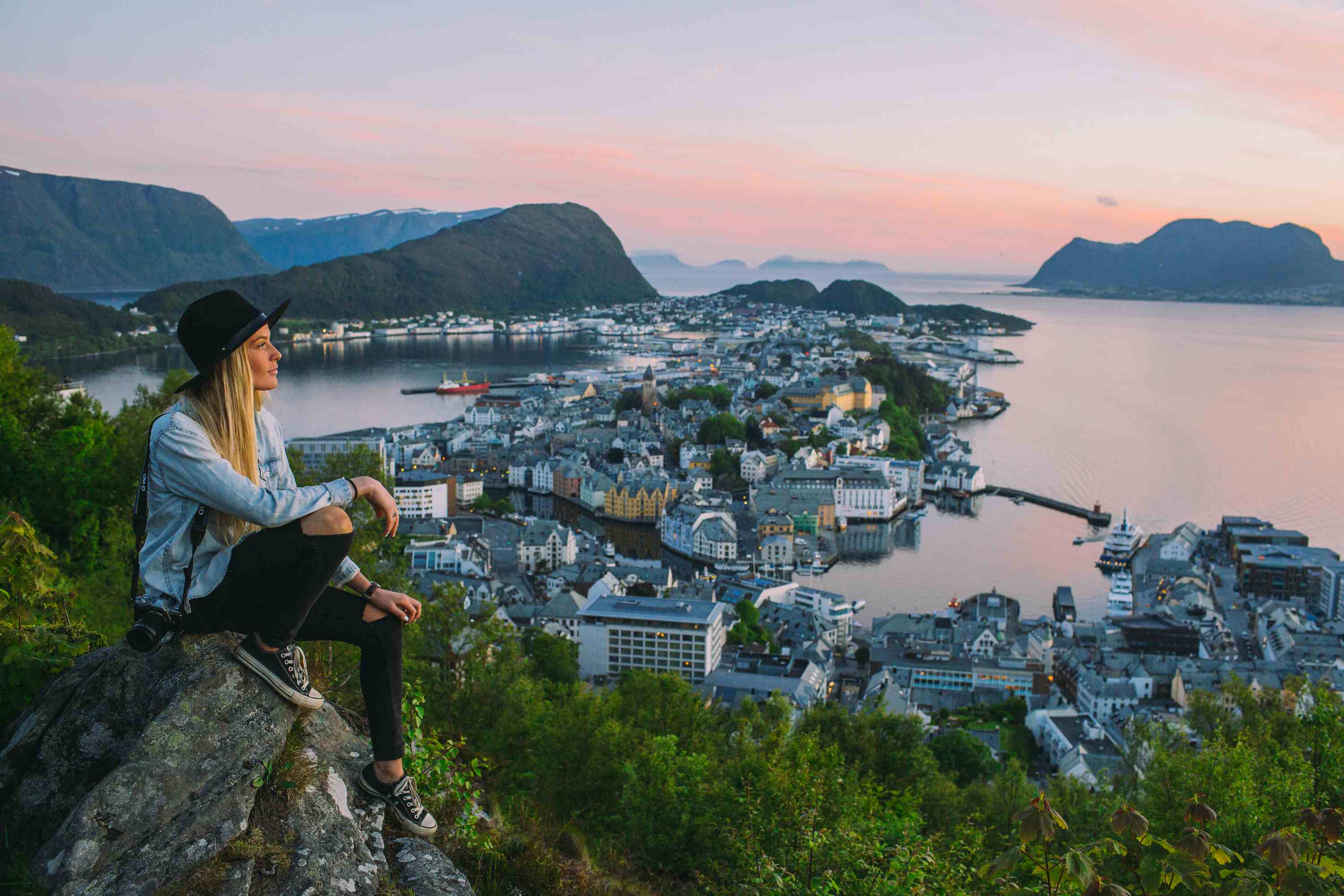 En kvinne som sitter på en stein og ser på utsikten utover Ålesund.