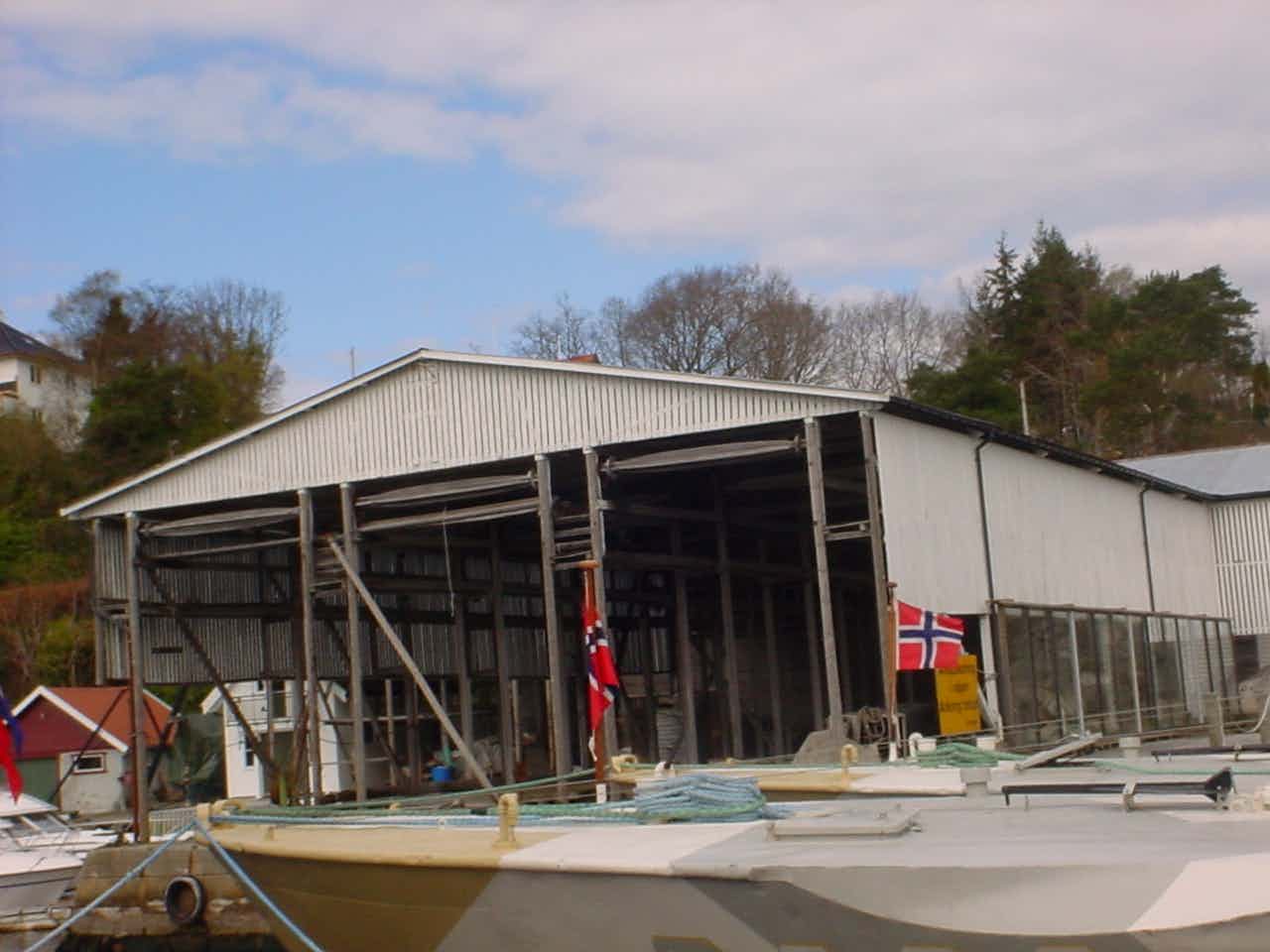 Historisk bygning ved sjø, båter, kai og hus.
