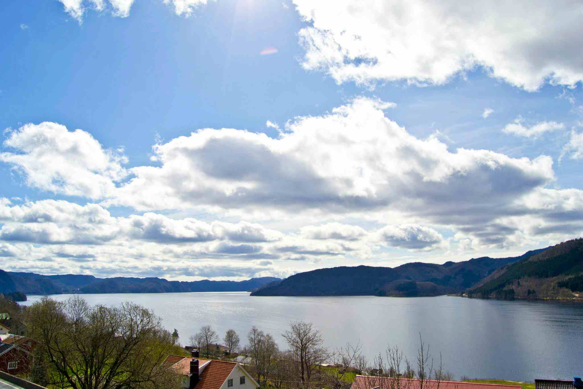 Hotellterrasse på Moi Hotell med utsikt over Lundevannet. Blå himmel med skyer og sol.