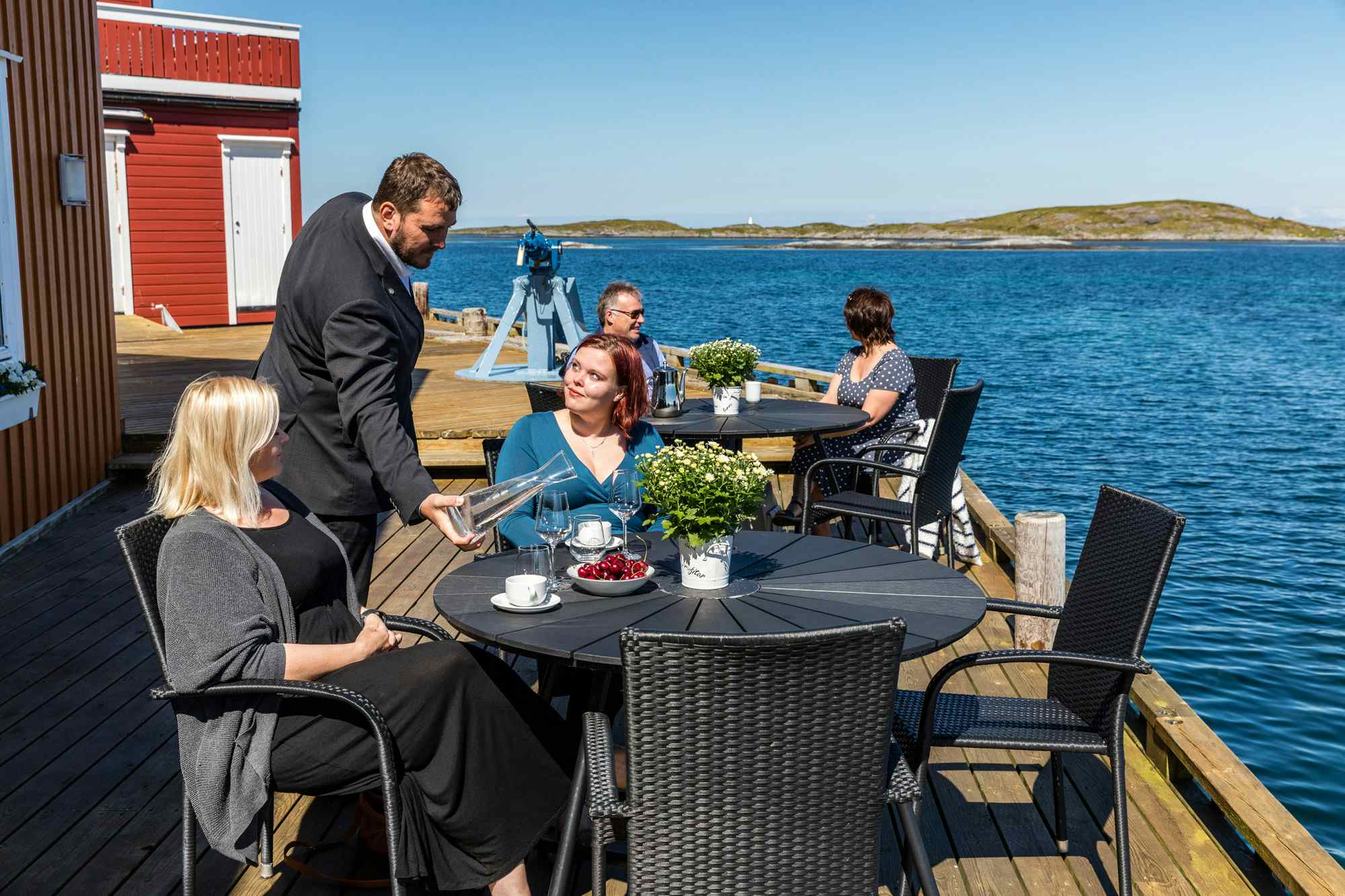 Personer får uteservering på bordene på brygga ved Finnøy Havstuer.