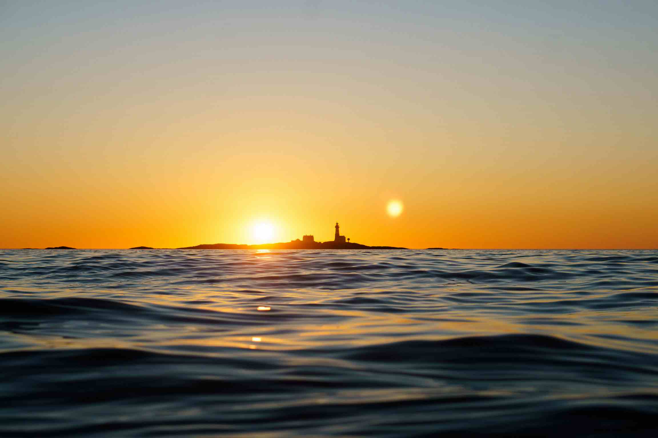 Person i vannet som kiter med solnedgangen bak seg. Bilder er i gulfarger pga. solnedgang