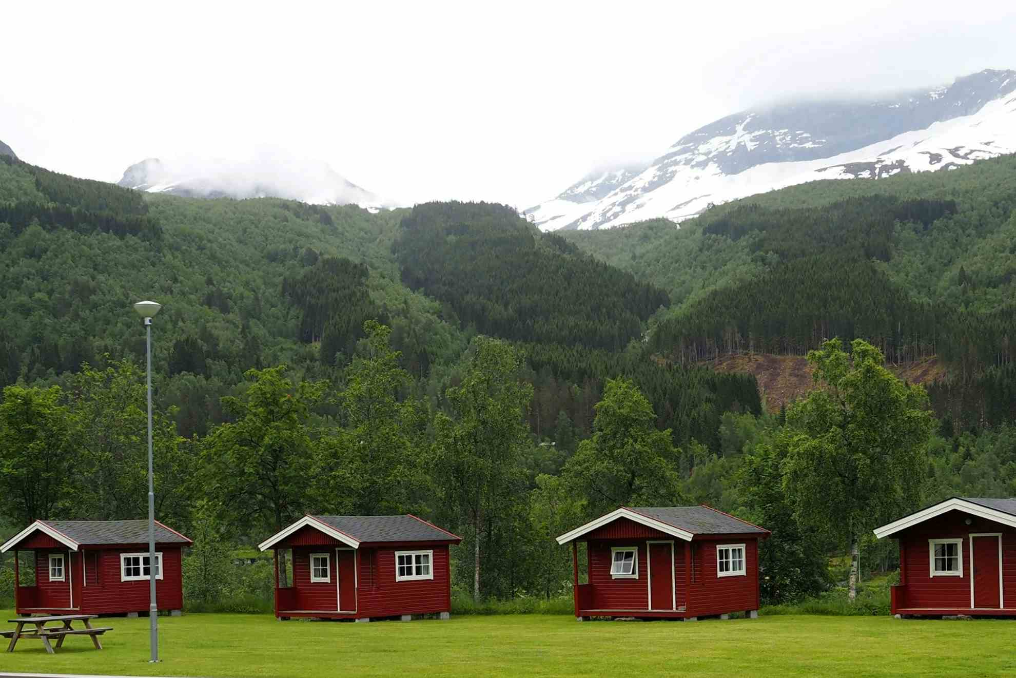 Små røde hytter på rekke på grønn mark hos Gjerde camping i Valldal