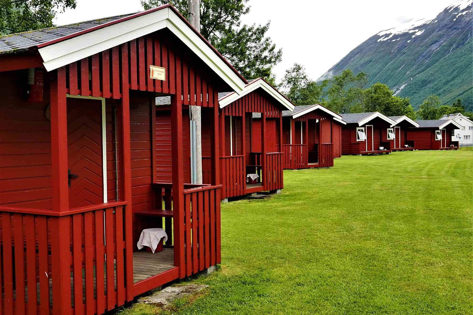 Små røde hytter på rekke på grønn mark hos Gjerde camping i Valldal