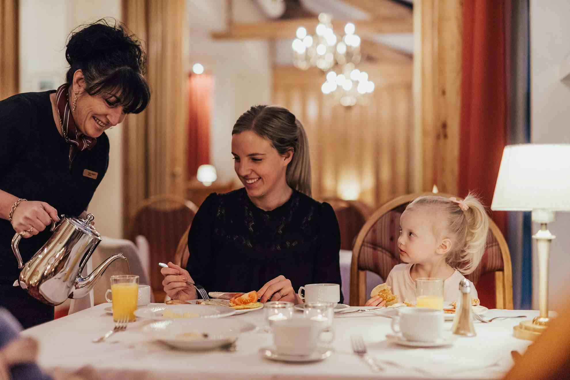Barn og voksen fosyner seg av et bugnende dessertbord på Hotel Union Geiranger i varme  omgivelser.