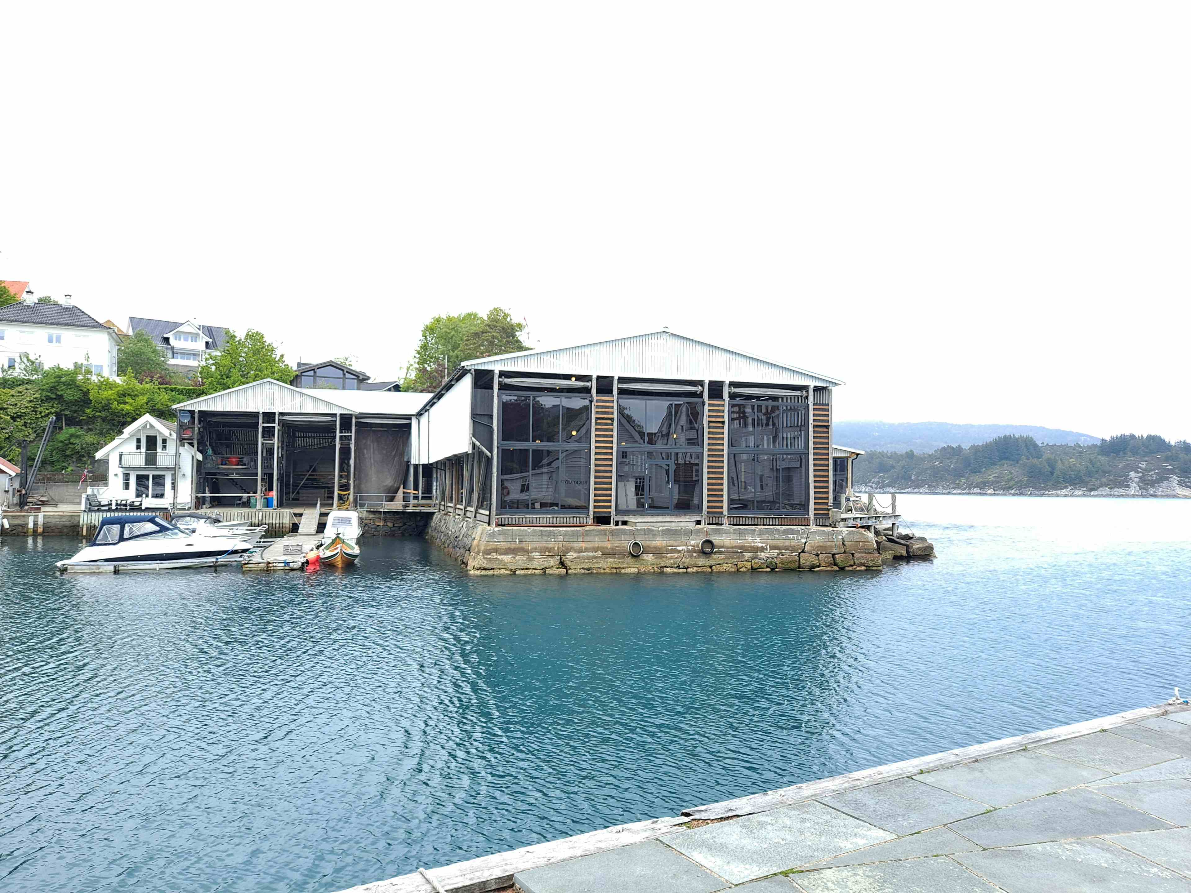 Historisk bygning ved sjø, båter, kai og hus.