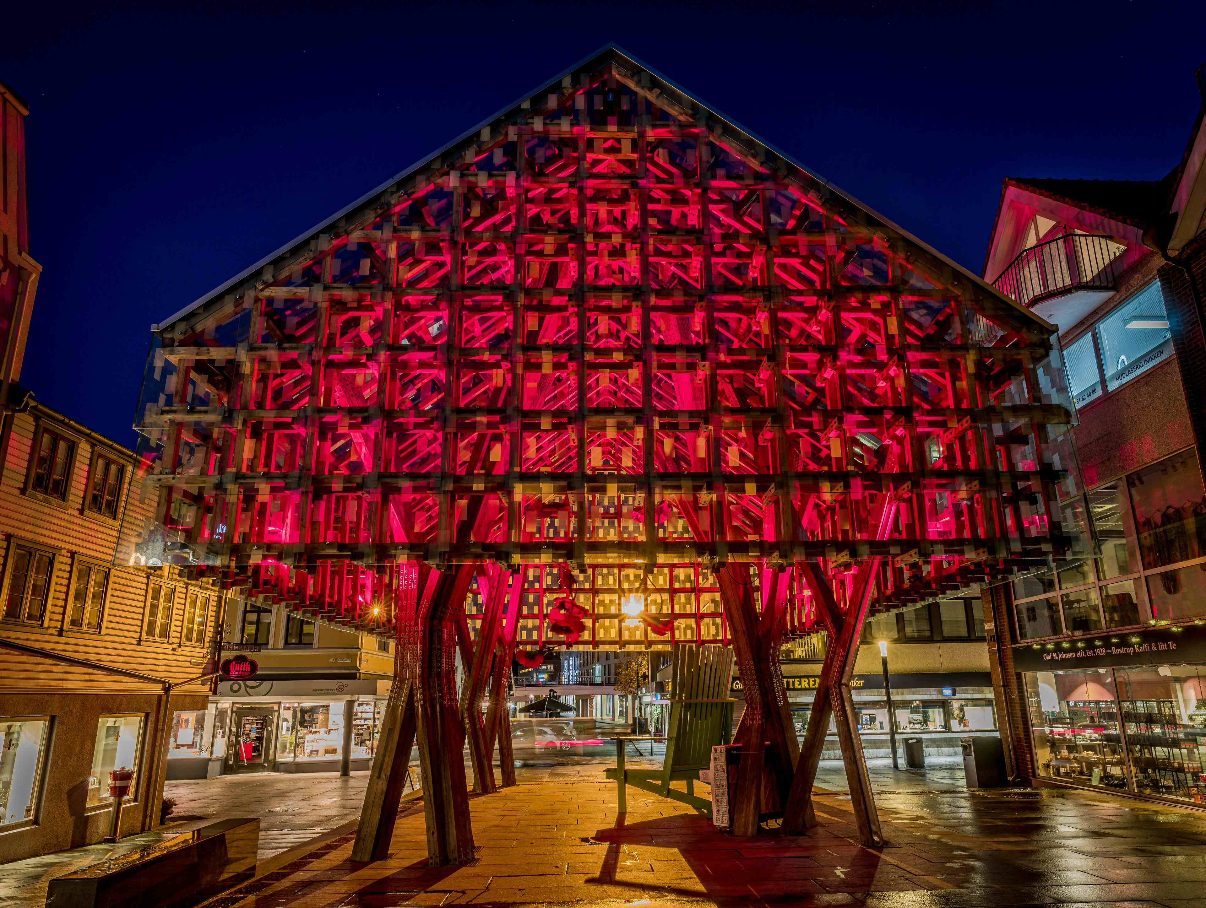 Et overbygg i glass og tre som kalles Lanternen som ligger i handlegaten i Sandnes. På bildet er det opplyst med røde lys. Det er mørkt og kveld.
