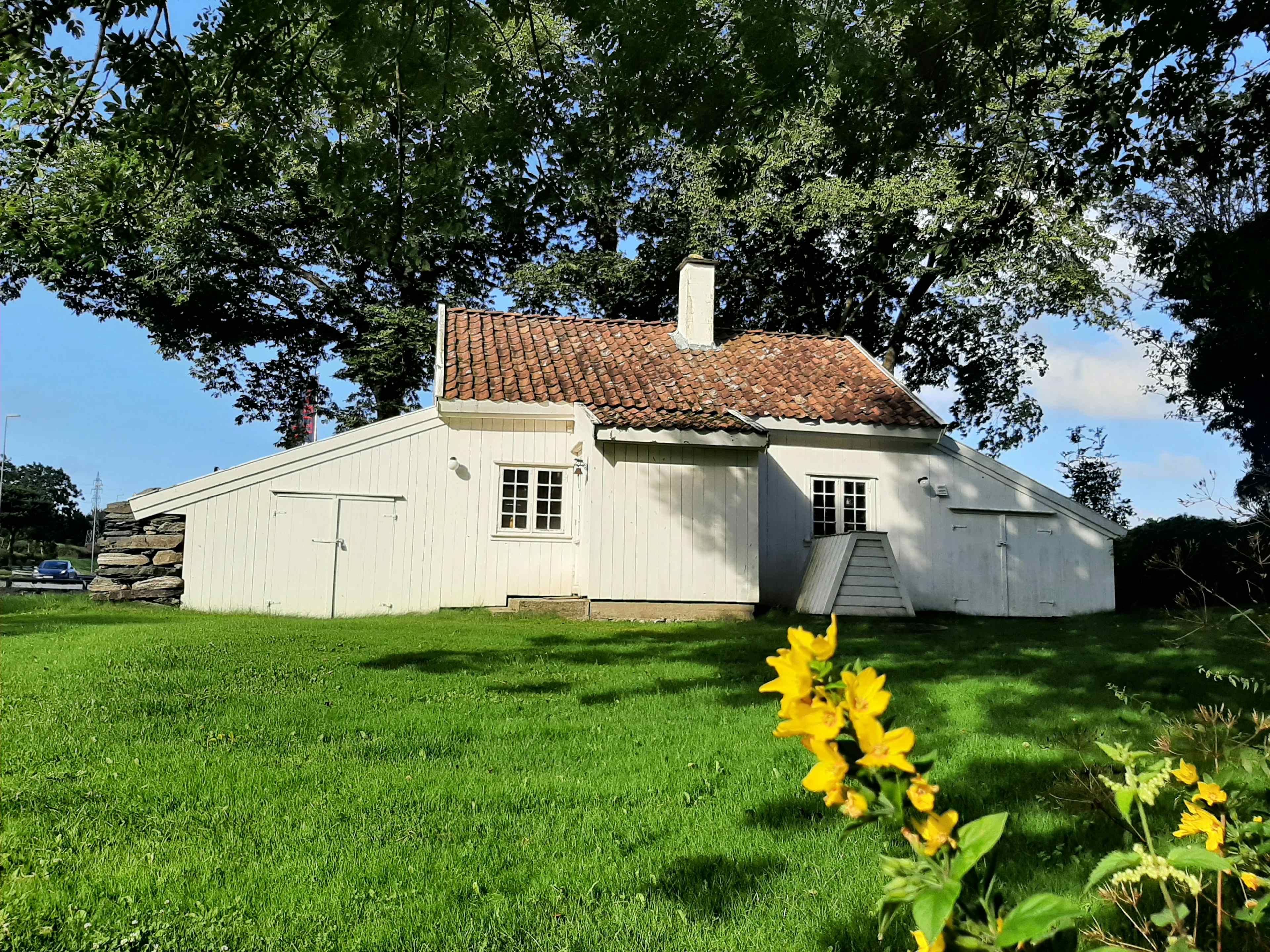 Kristinahuset, et jærhus i tradisjonell byggeskikk ligger på en grønn gressplen med trær rundt.