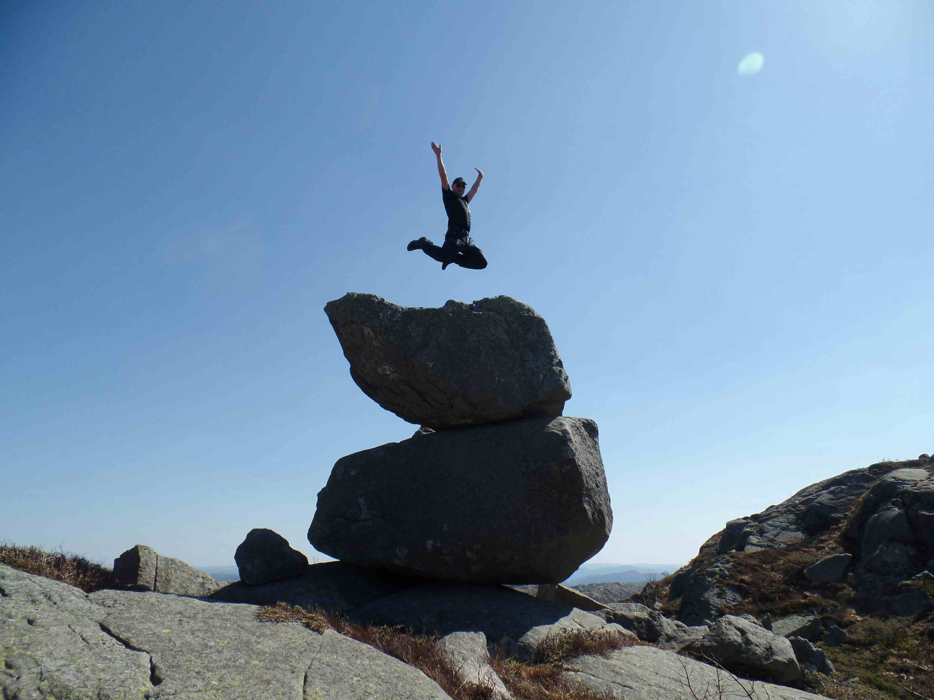 Person som hopper på toppen av et fjell med store steinblokker. Hattesteinan