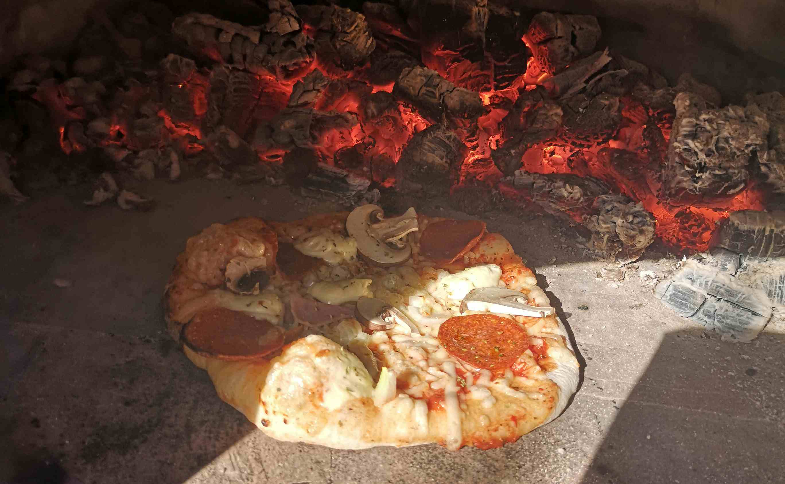 Pizza med salami og champignon som stekes i steinovn med rødglødende kull.
