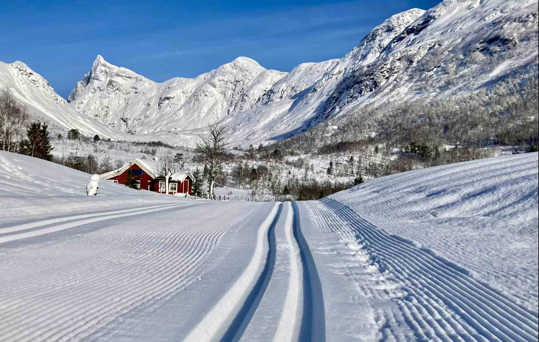 Person renn på ski ned skiløypa omkransa av høge fjell i vinterdrakt.