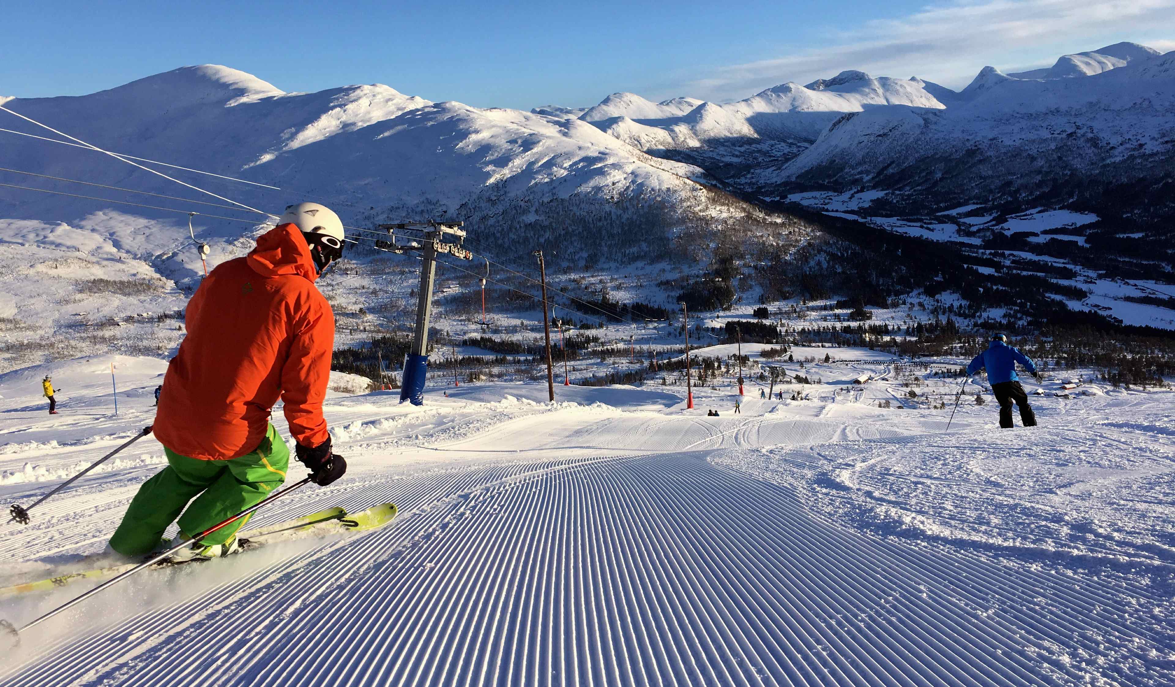 Person renn på ski ned skiløypa omkransa av høge fjell i vinterdrakt.