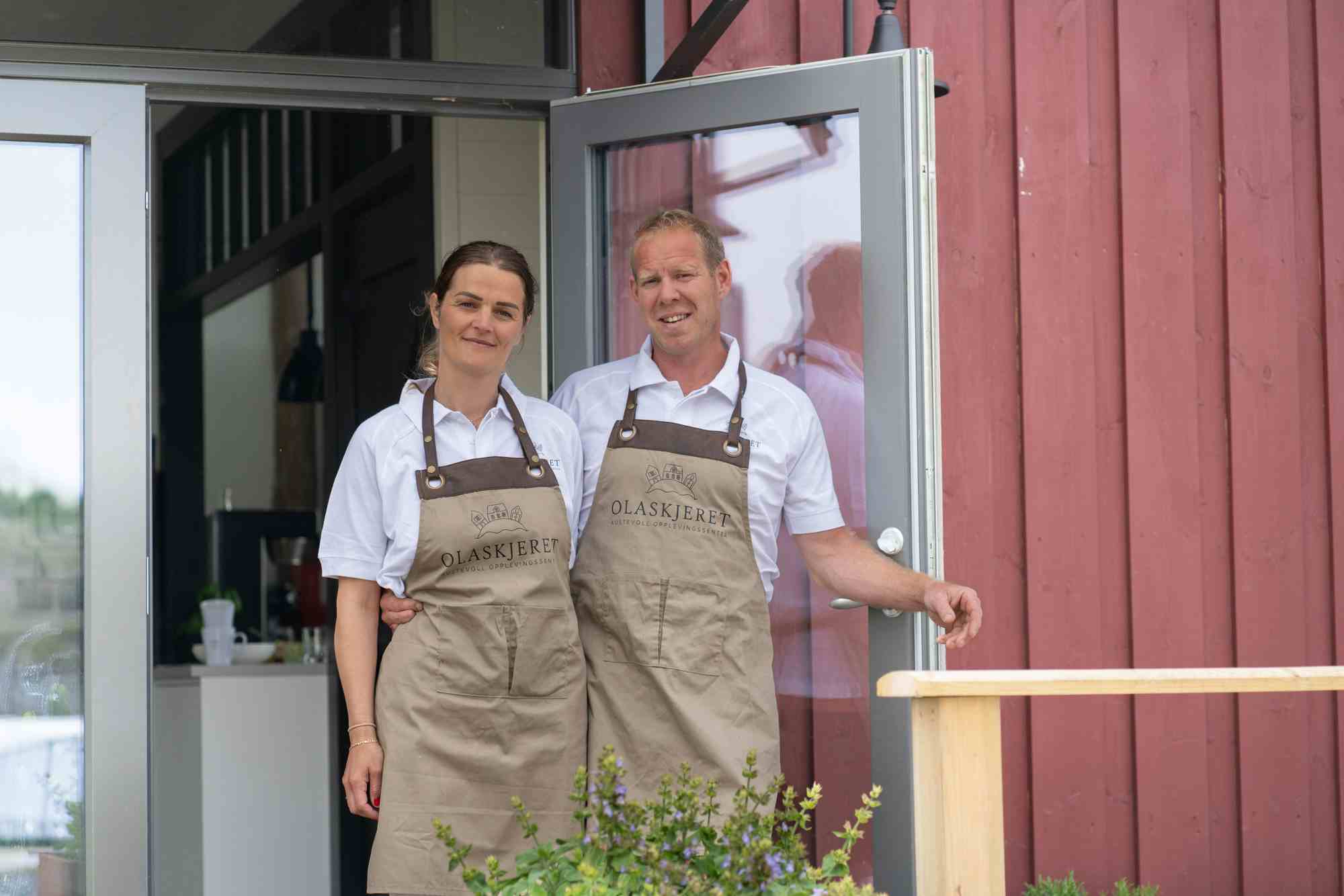 To personer i hvite t-skjorter og brune forkle som står i åpen dør på restaurant. Foto.