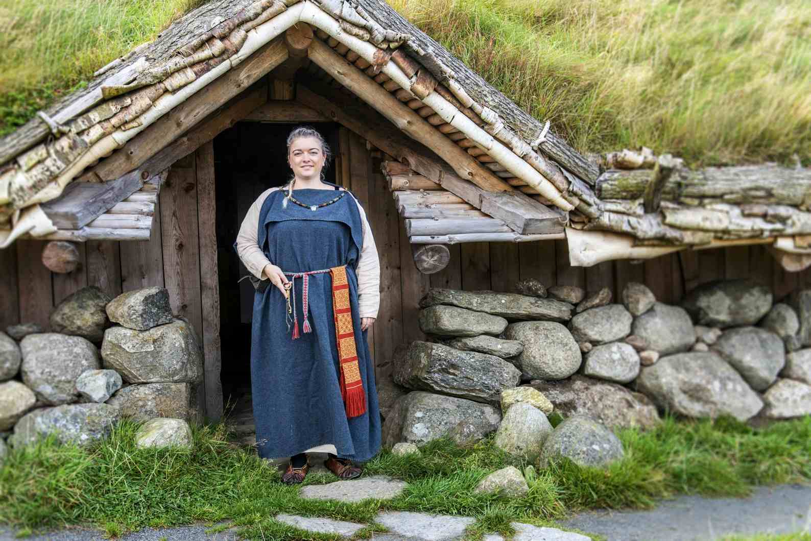 Woman standing in the doorway of a longhouse from the iron age. Dressed in period clothing.