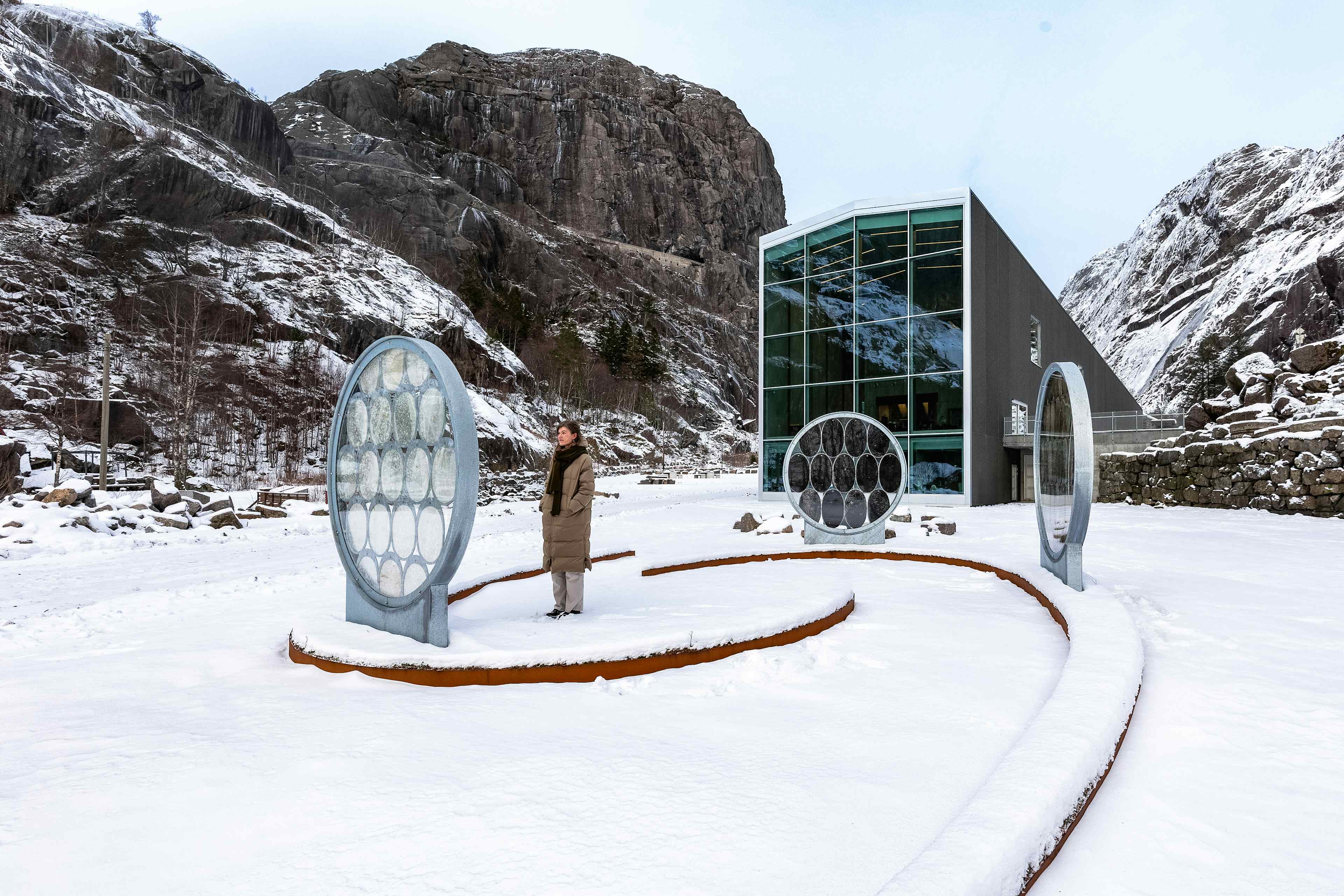 Artwork in front of a museum building - there is snow on the ground. A person is standing watching the artwork.