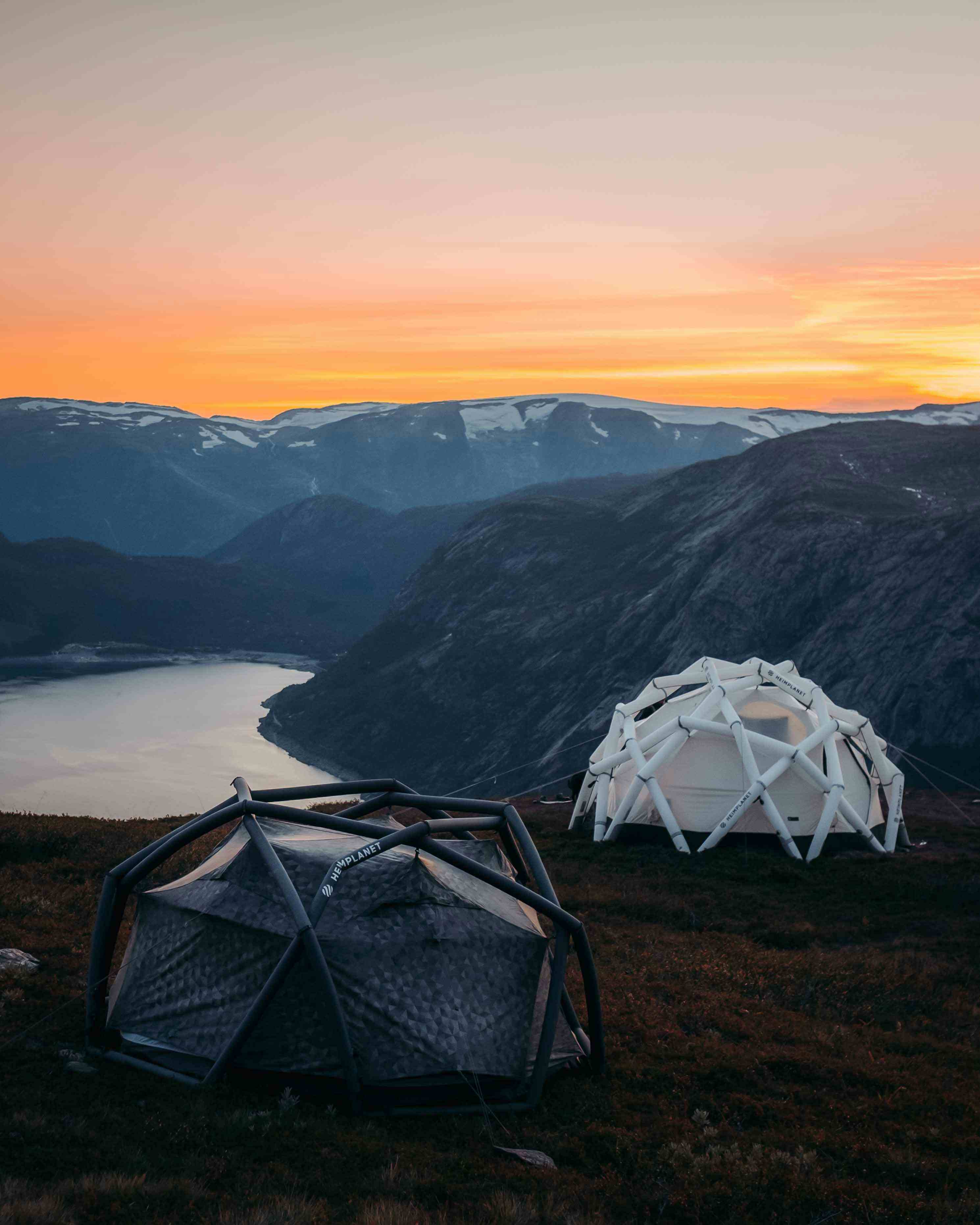 Bålpanne med åpen ild på en fjelltopp ved solnedgang med utsikt over en fjord.