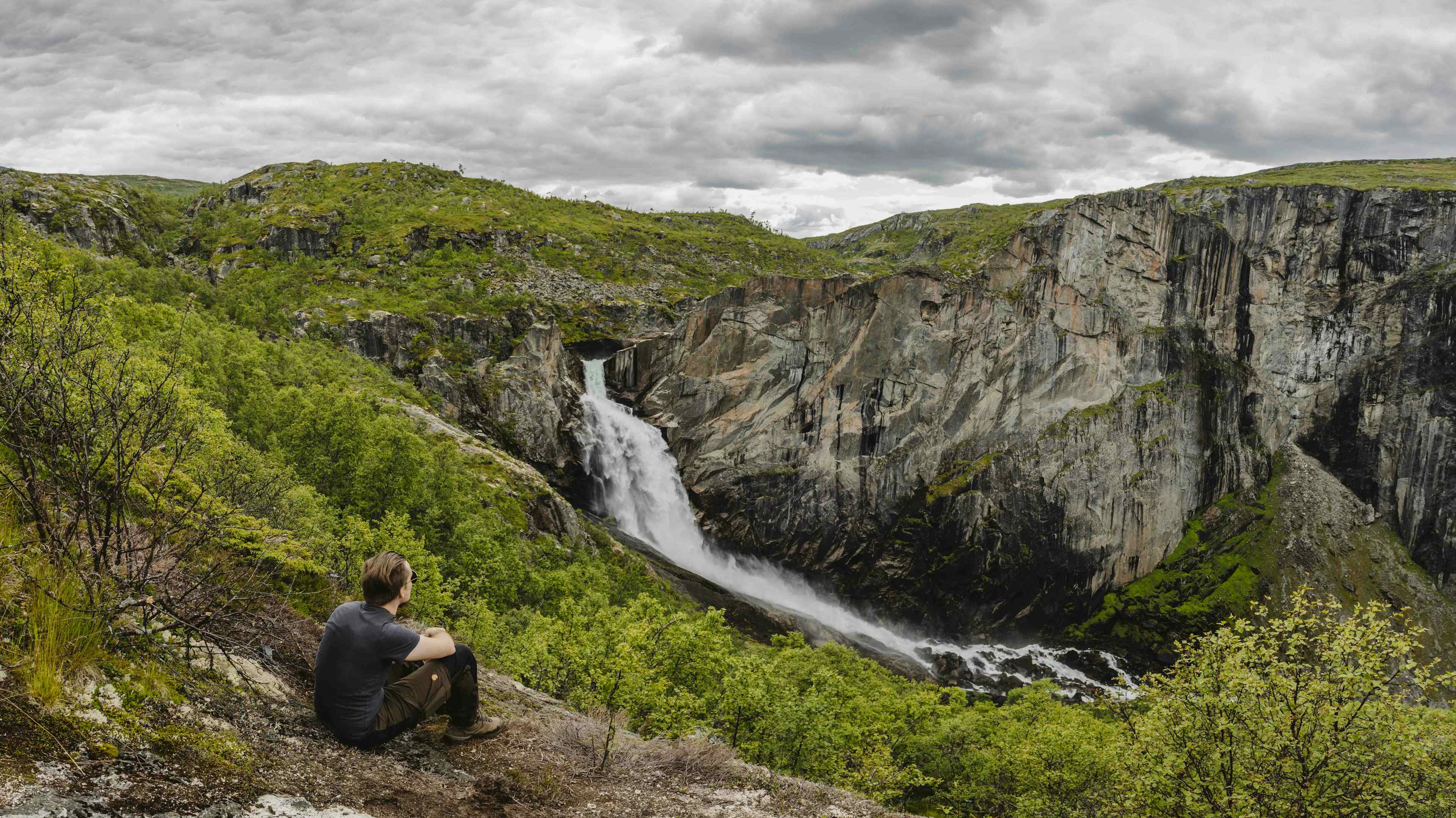 En mann sitter på bakken og ser på Valurfossen nedenfor.