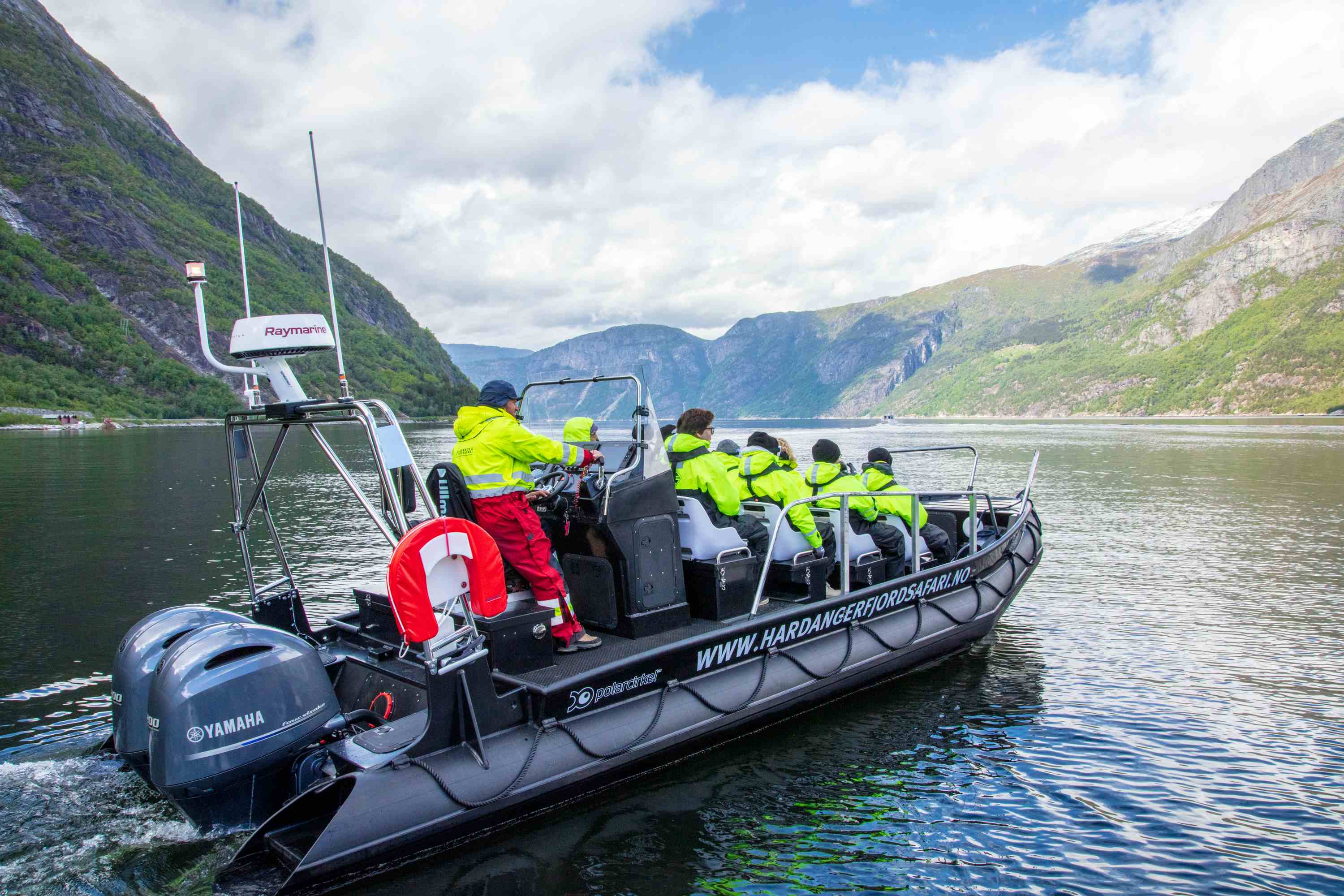 En ribbåt fylt med passasjerer i fart langs fjorden.