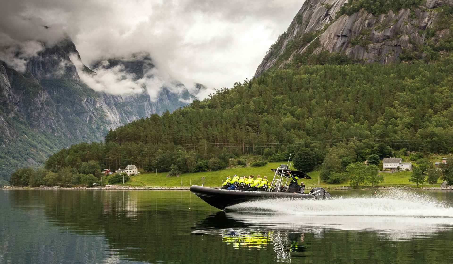 En ribbåt fylt med passasjerer i fart langs fjorden.