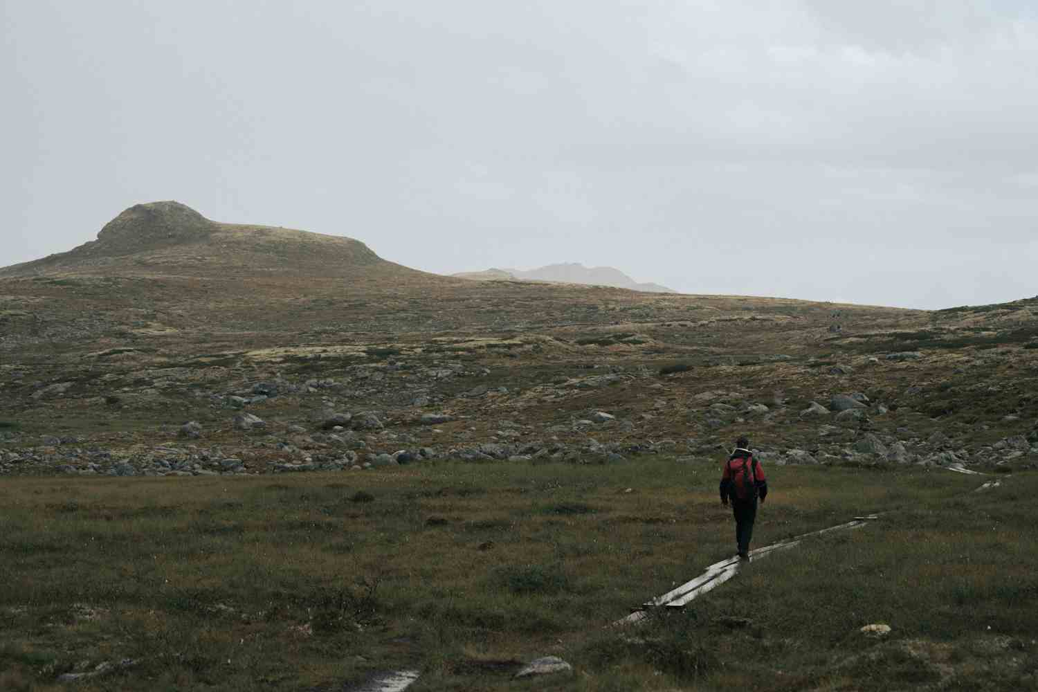 En turgåer står på toppen av en ås og ser ned mot Rauhelleren Turisthytte.