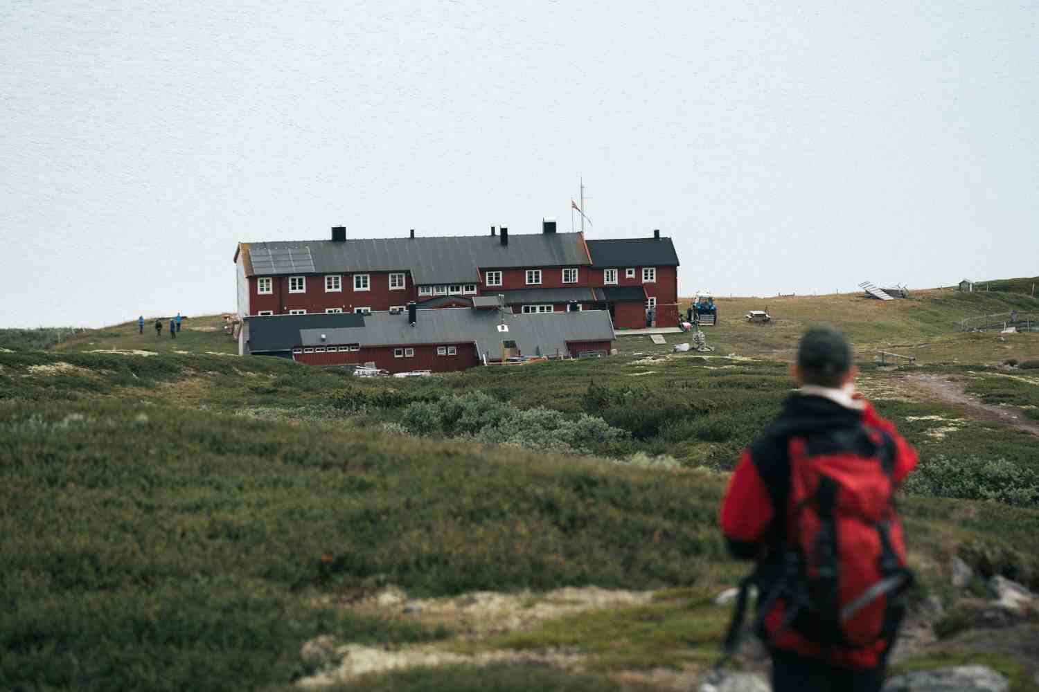 En turgåer står på toppen av en ås og ser ned mot Rauhelleren Turisthytte.