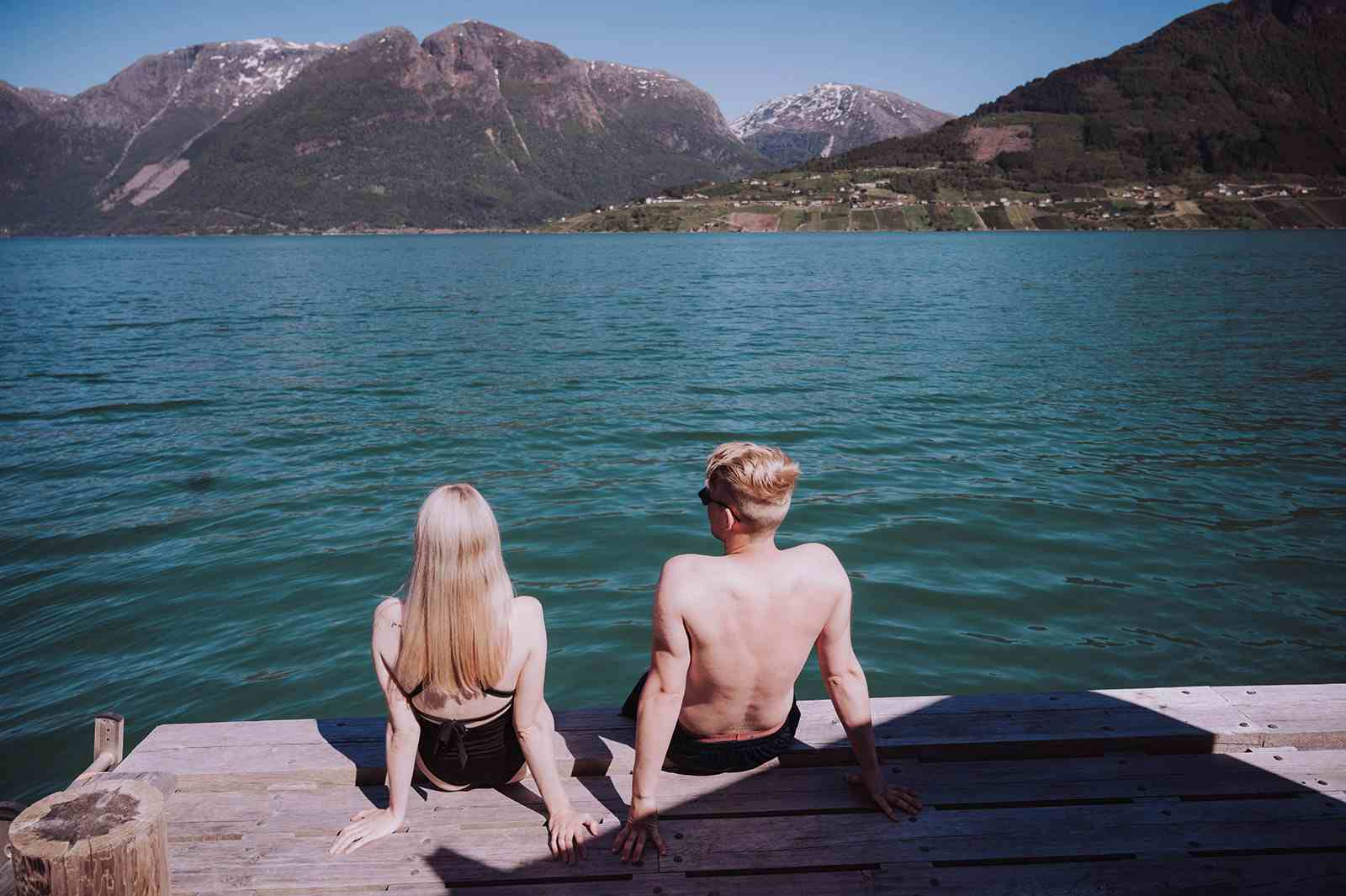 Personer nyter fjordbad på brygge foran Heit Grimo sauna med fjell i bakgrunnen