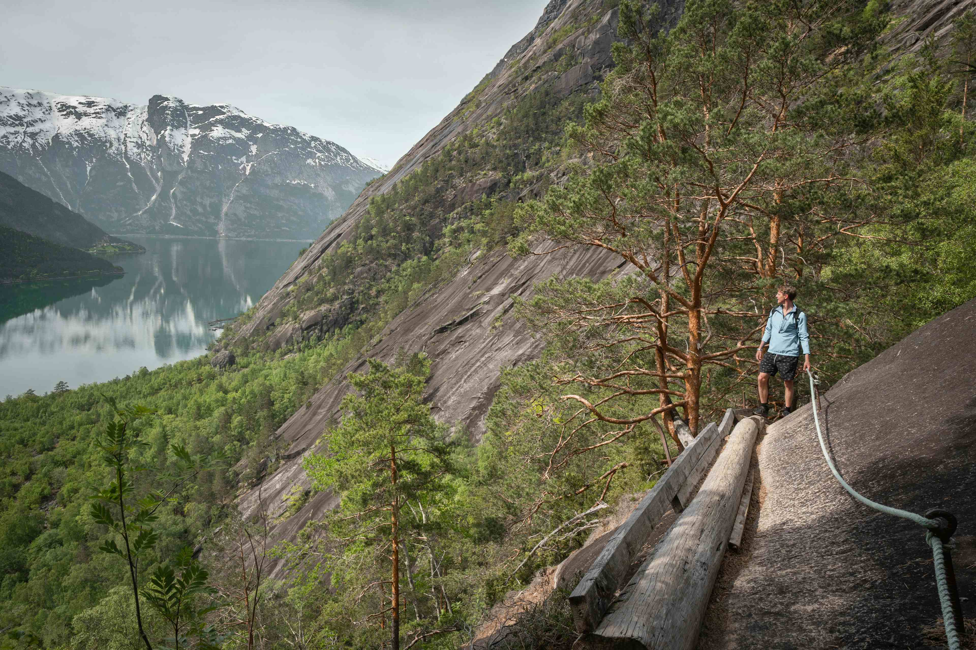 En kvinnelig turgåer som går på trestien boltet inn i fjellveggen ved siden av fjorden.