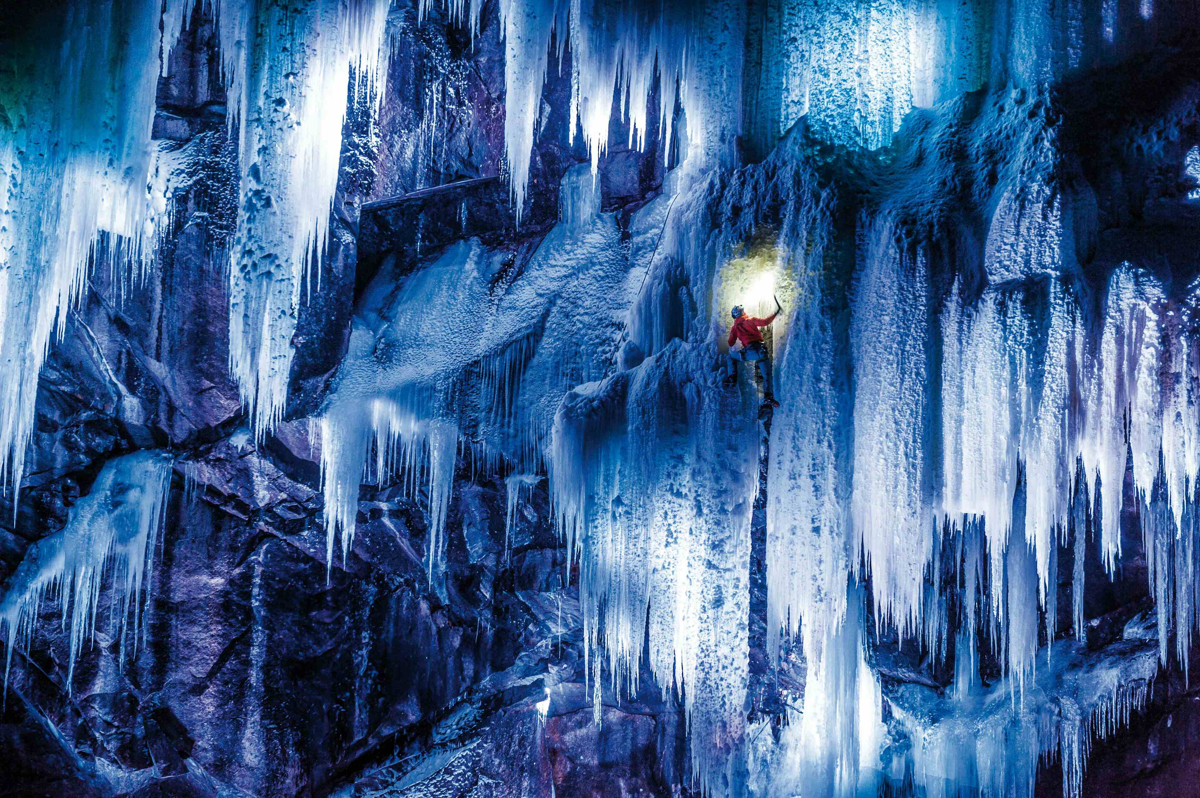 En isklatrer i rød jakke sett nedenfra klatrer den turkisfargede isen.