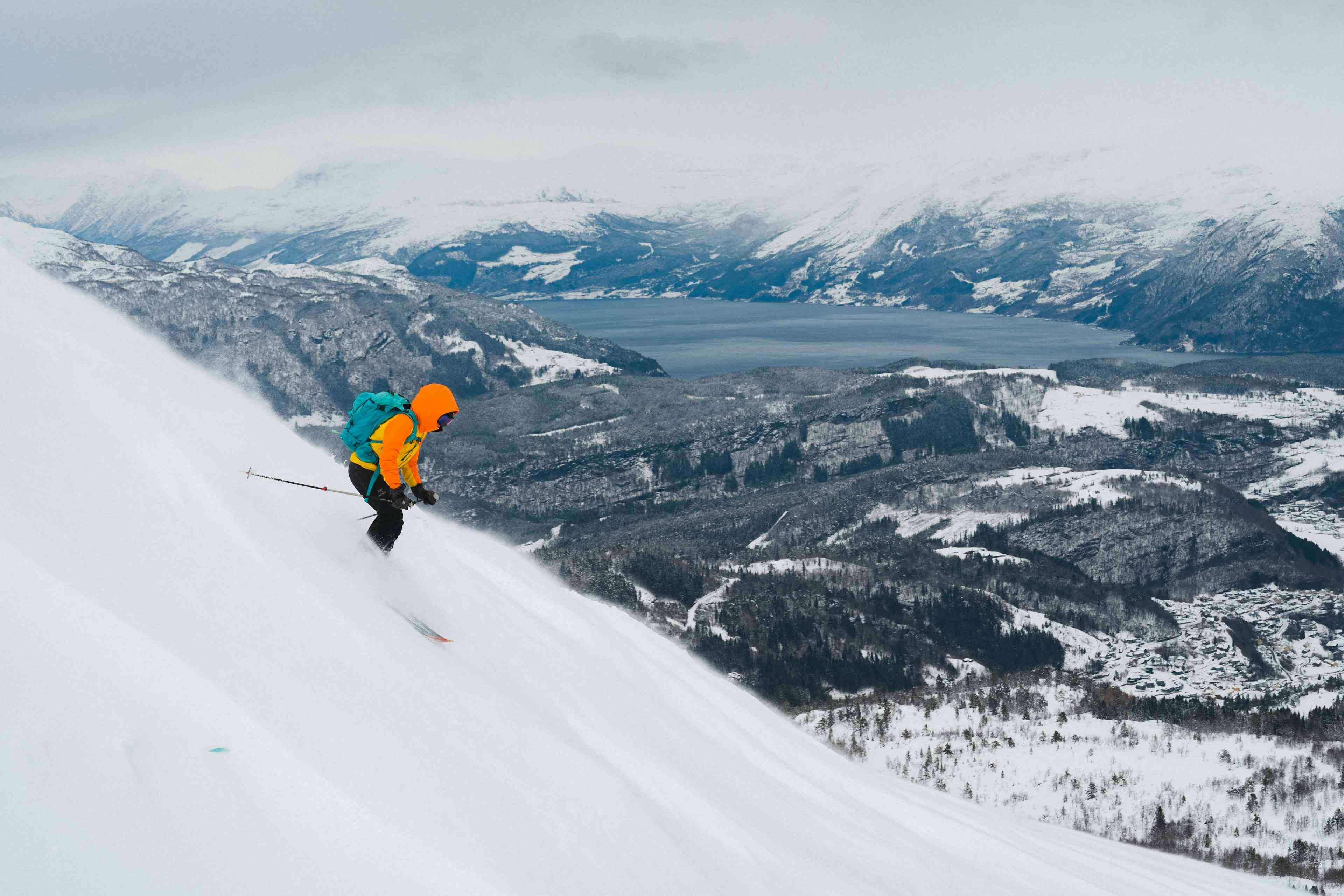 Topptur i Hardanger. Skikjører hopper ned en fjellside med utsikt mot Hardangerfjorden og snødekket landskap.