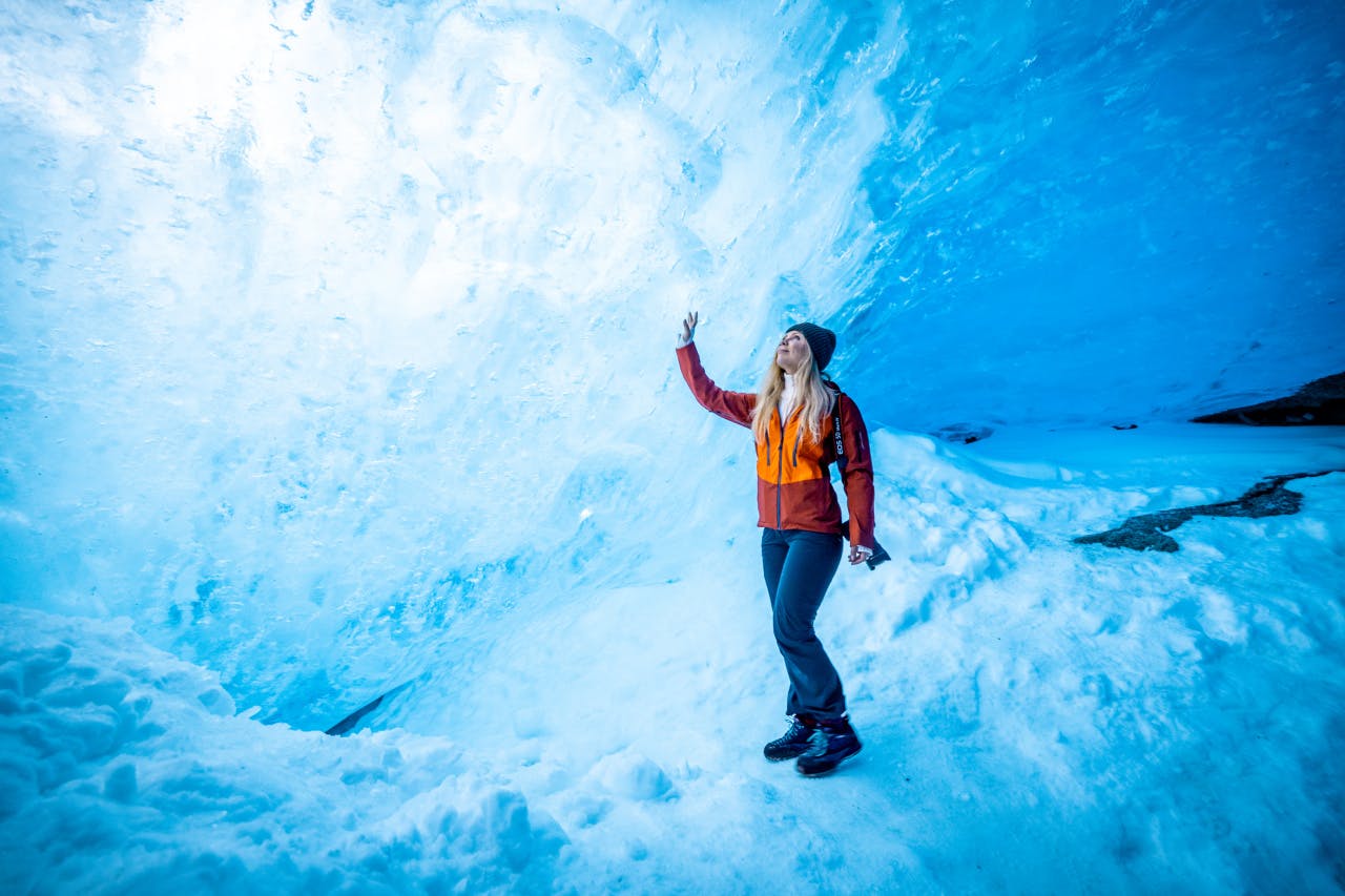 Winter in fjord norway, a woman in a blue, ice cave looking around. 